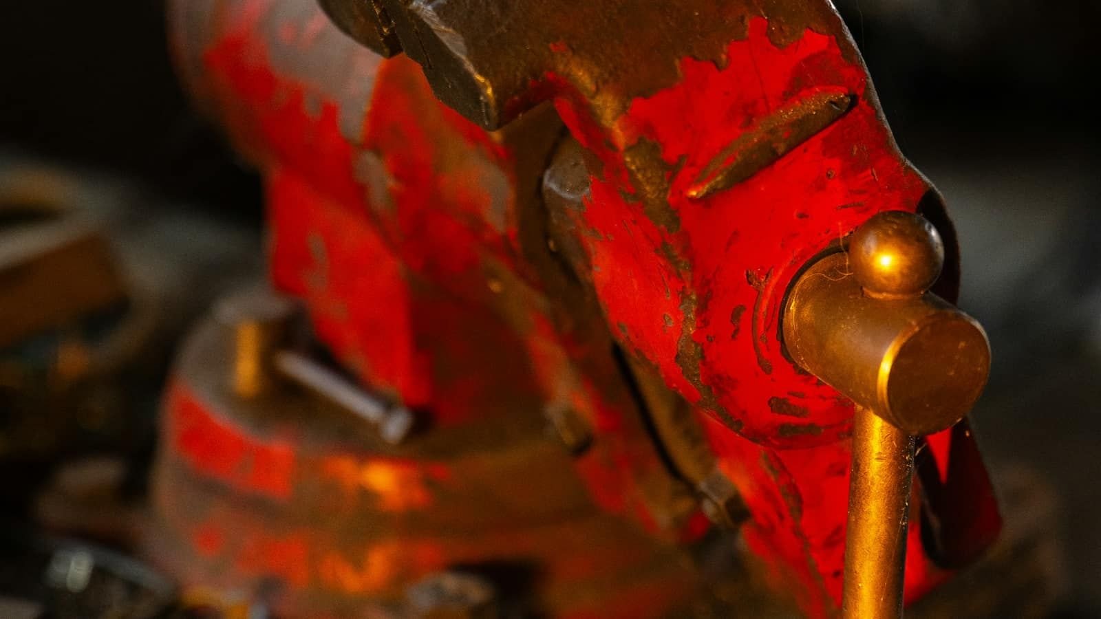 A worn red metal vise on a workshop bench