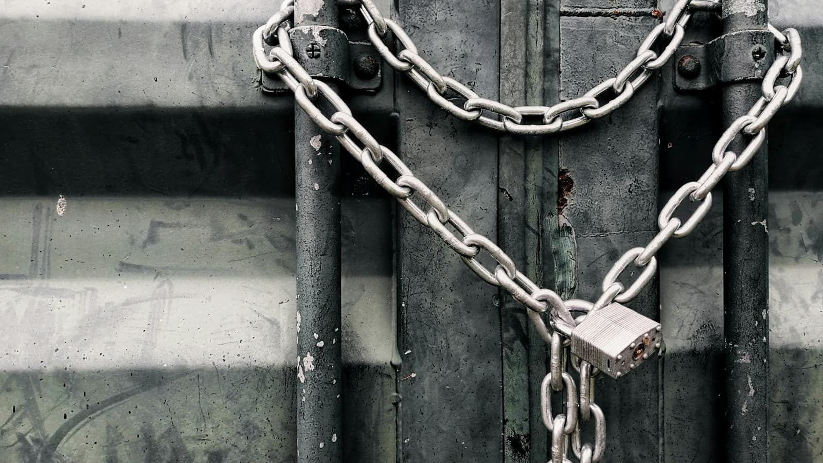 A heavy steel chain and padlock holding a grey metal door shut