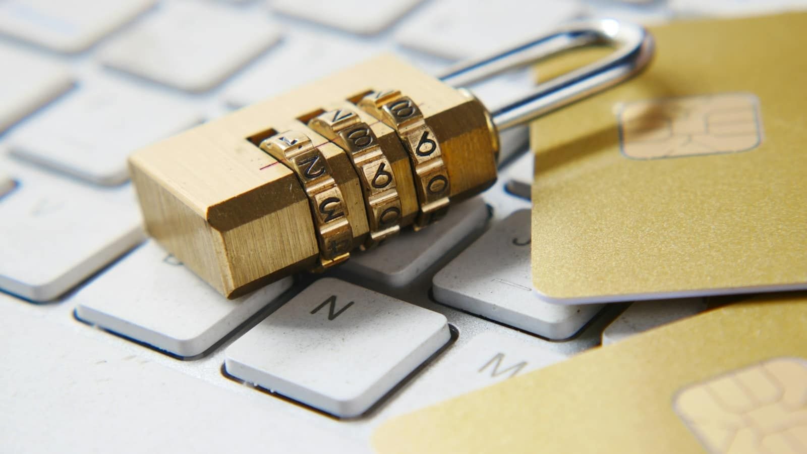 A gold combination padlock and two bank cards lying on a white keyboard