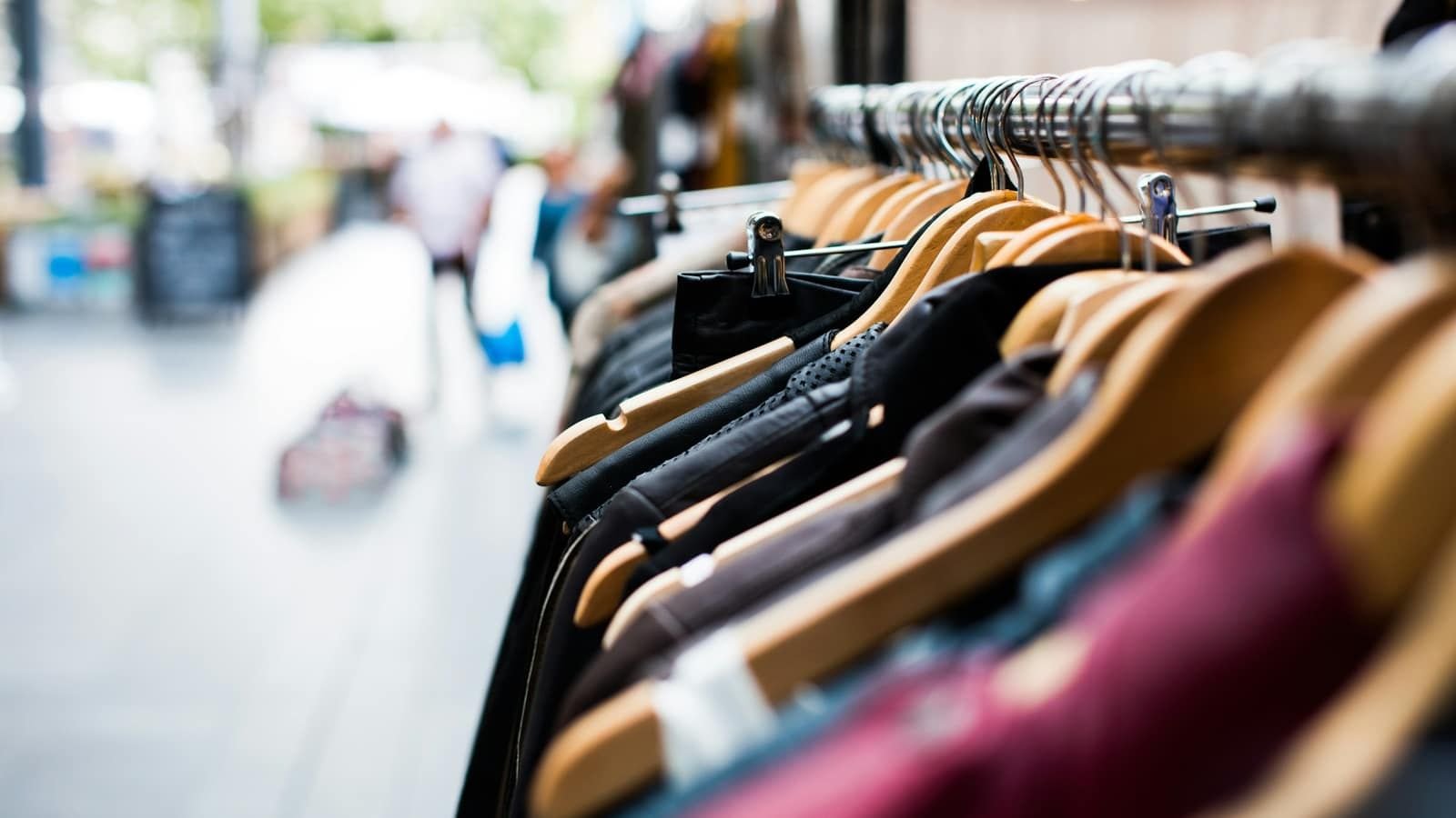 A rail of second-hand clothes on wooden hangers at an outdoor market