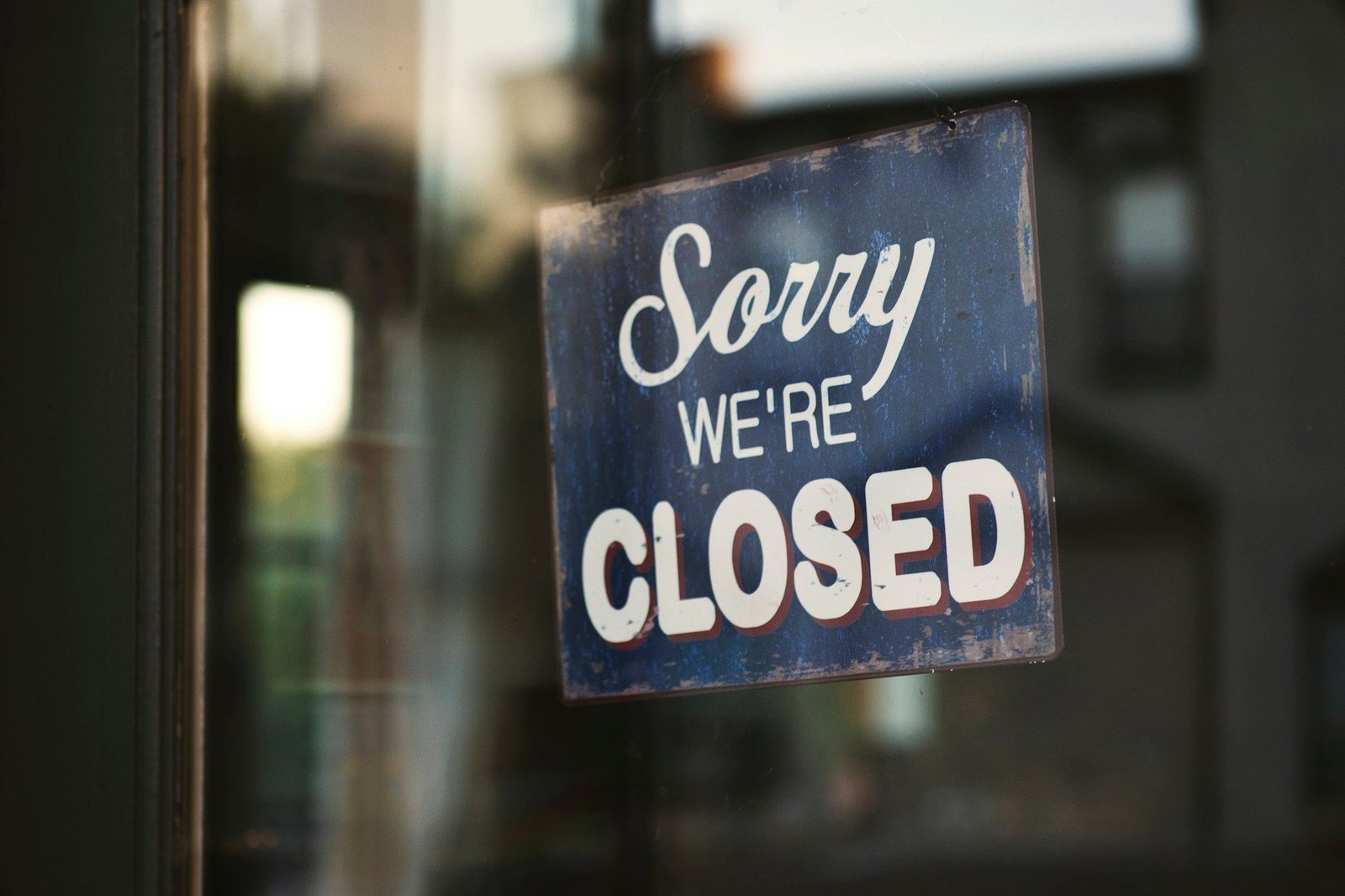 A blue "Sorry, we're closed" sign hanging in a shop's glass door