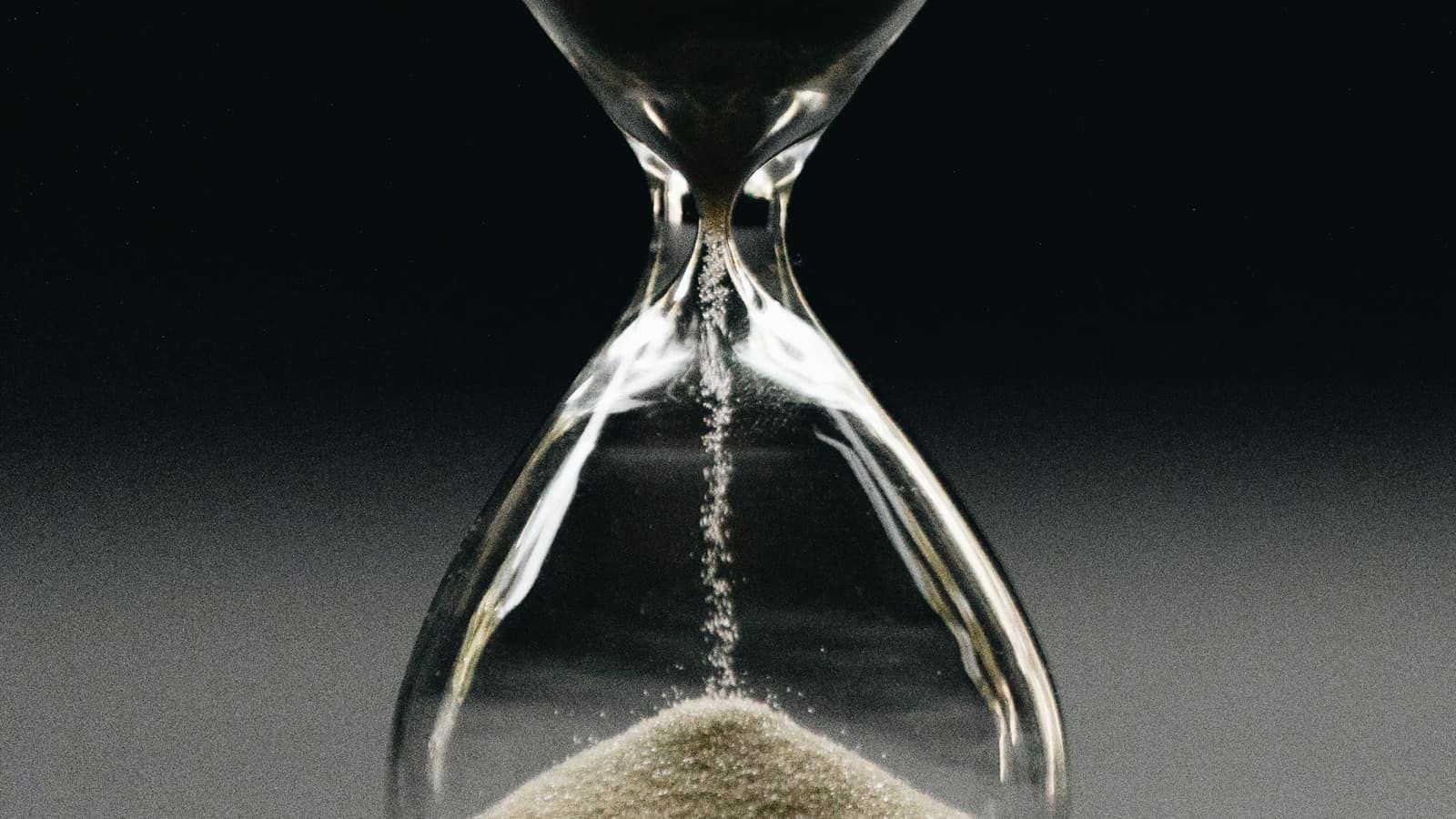 Sand running through a glass hourglass against a dark background