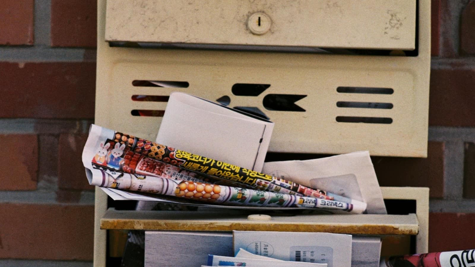 An old wall mailbox stuffed with letters and newspapers
