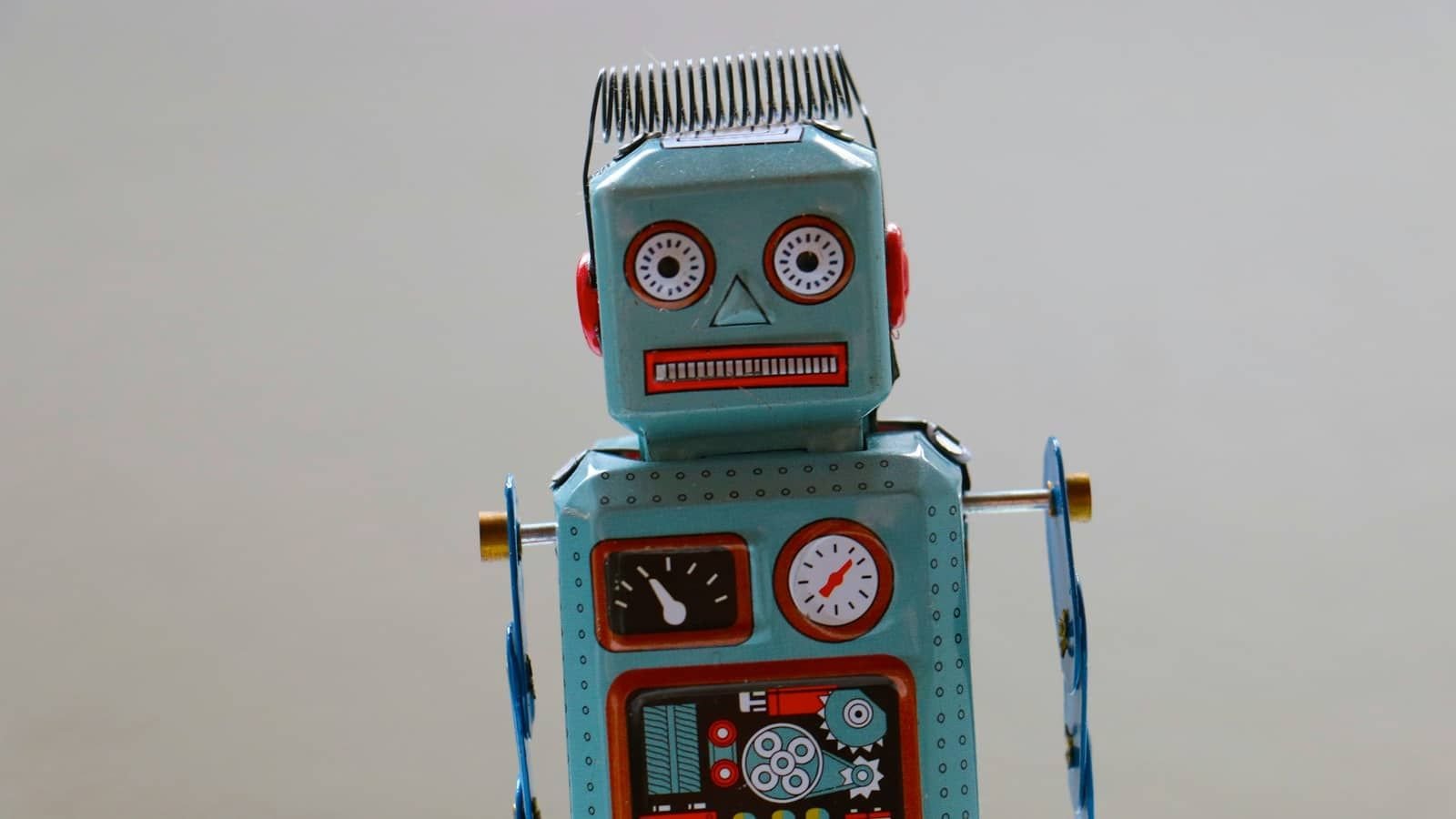 A blue vintage tin robot toy with round red eyes against a grey background