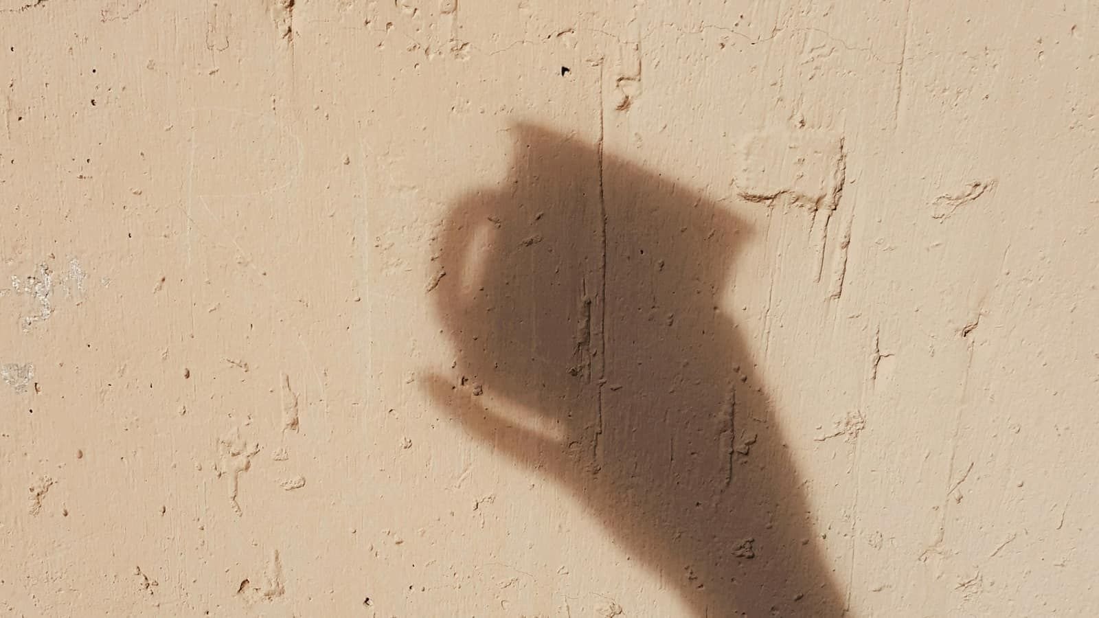 The shadow of a hand holding a phone cast on a sandy plaster wall