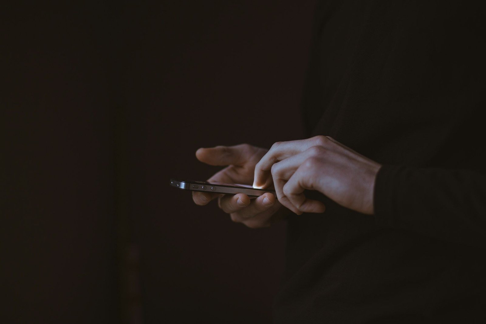 Two hands holding a smartphone in a dark room