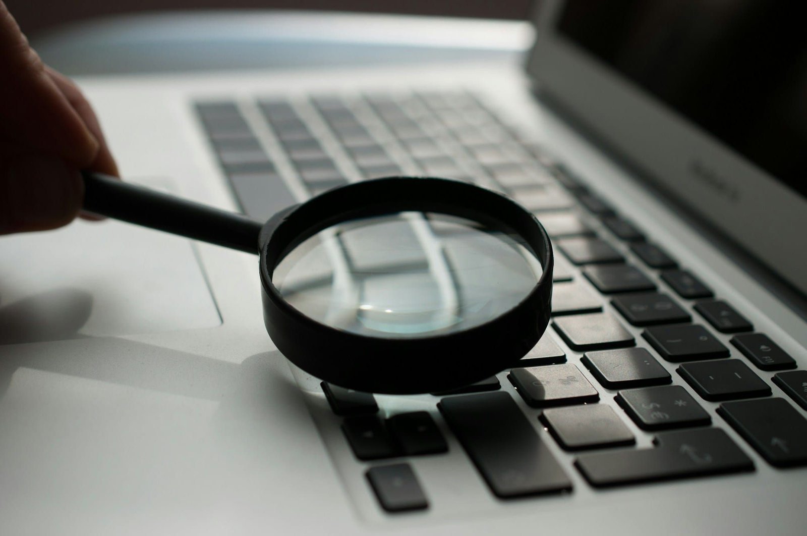 A magnifying glass held over the keyboard of a grey laptop