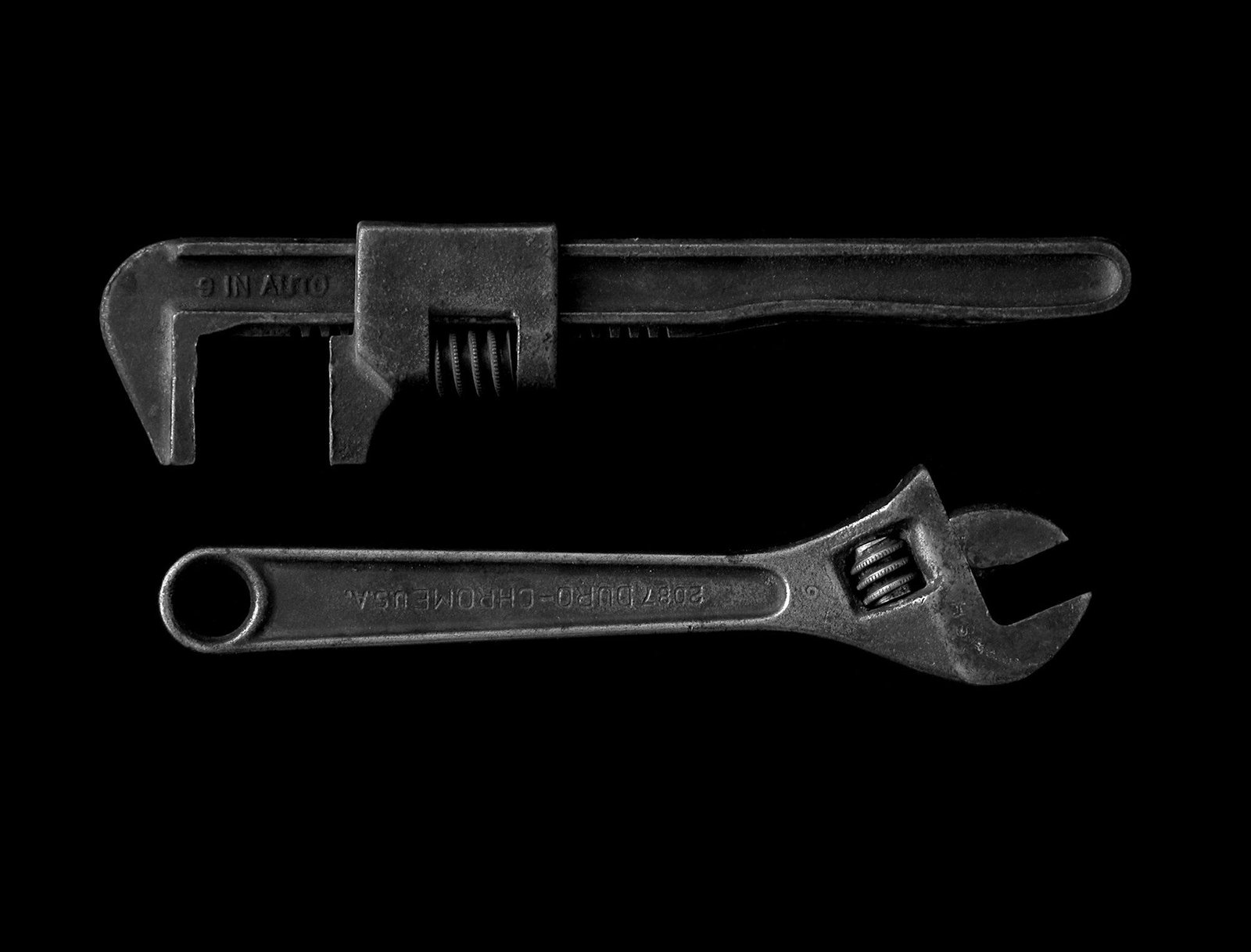 A pipe wrench and an adjustable wrench lying on a black background