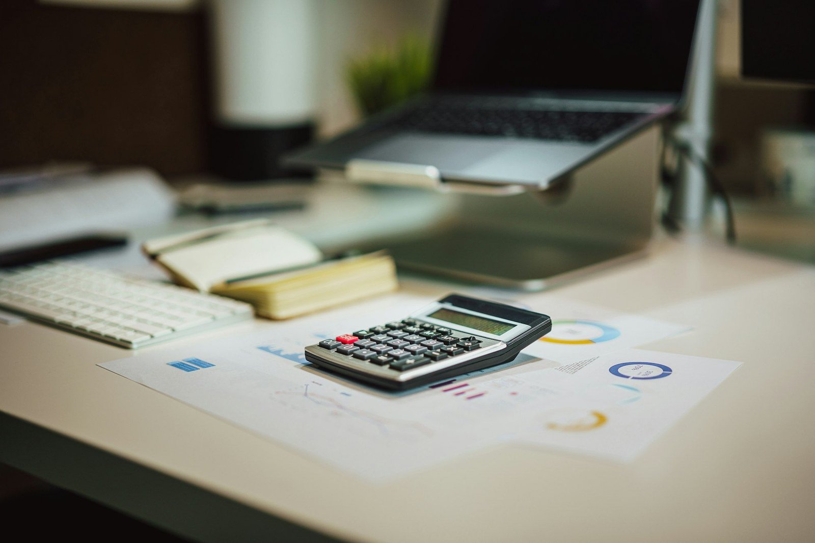 A desk calculator next to an open laptop on a white office desk