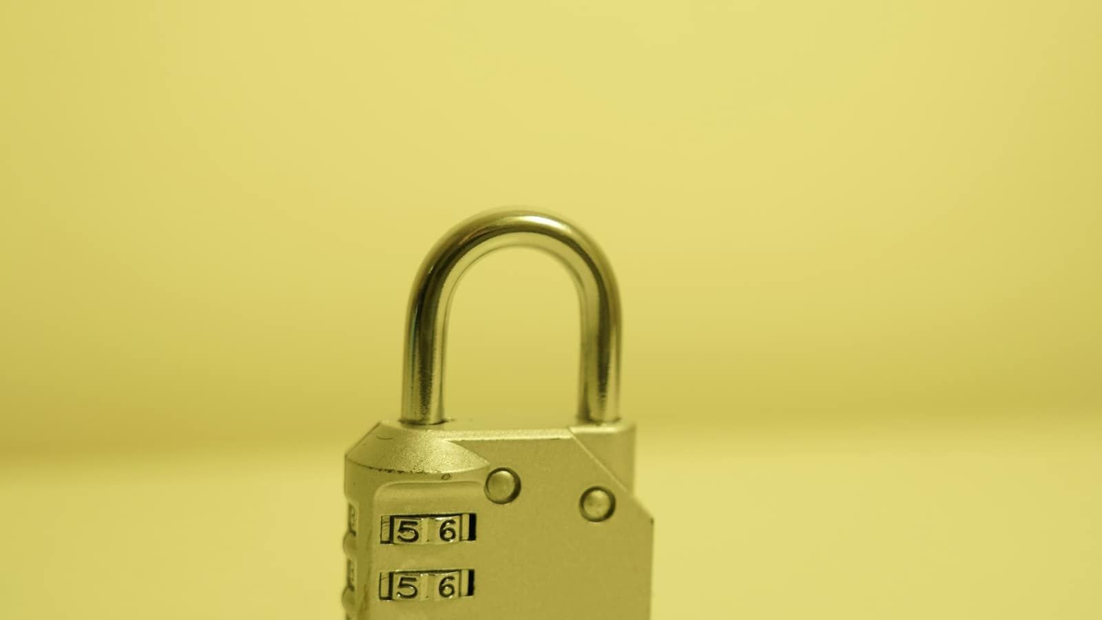 A small silver combination padlock against a plain yellow background