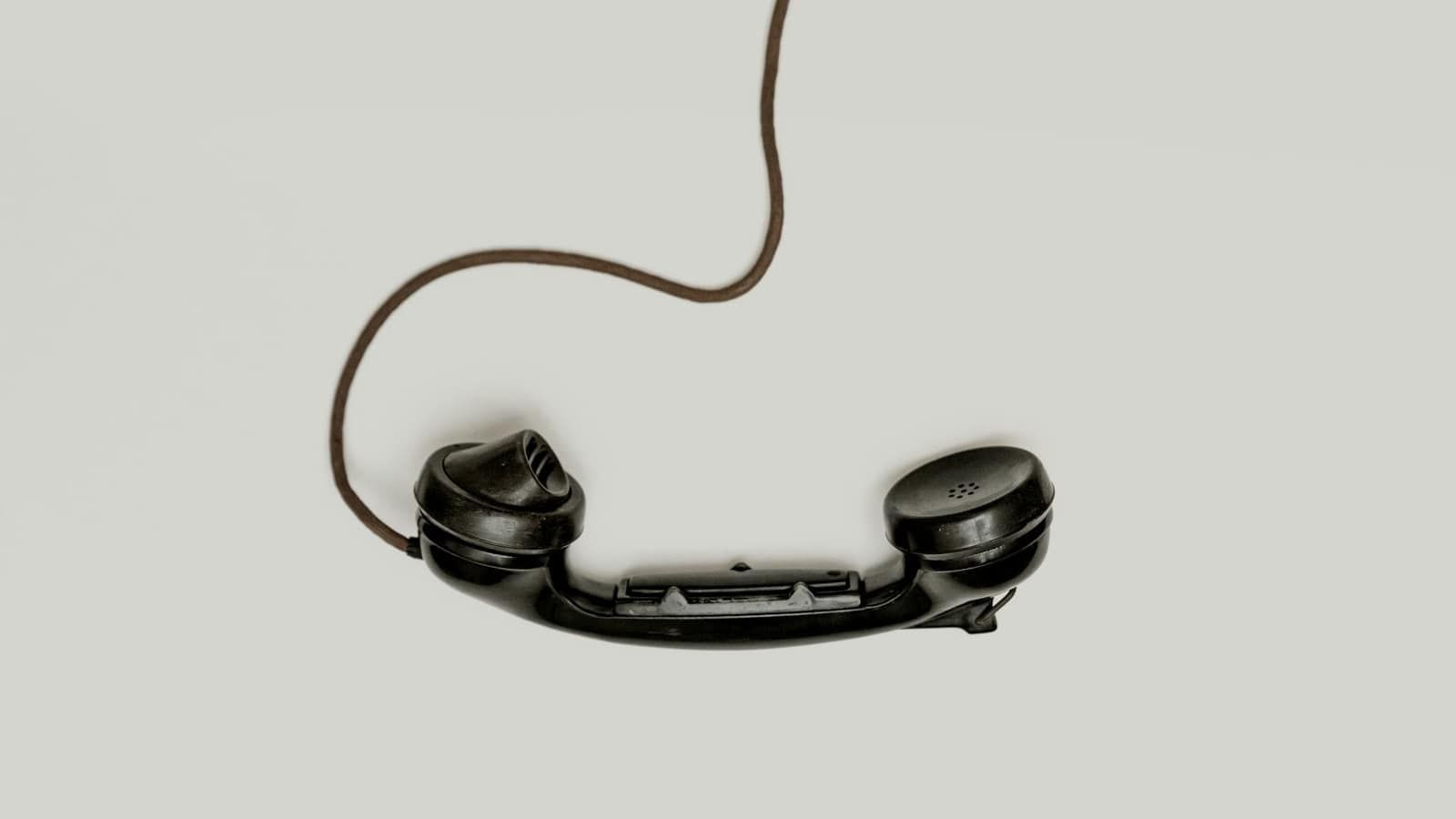 An old black telephone handset lifted off the hook, its cord curling above it