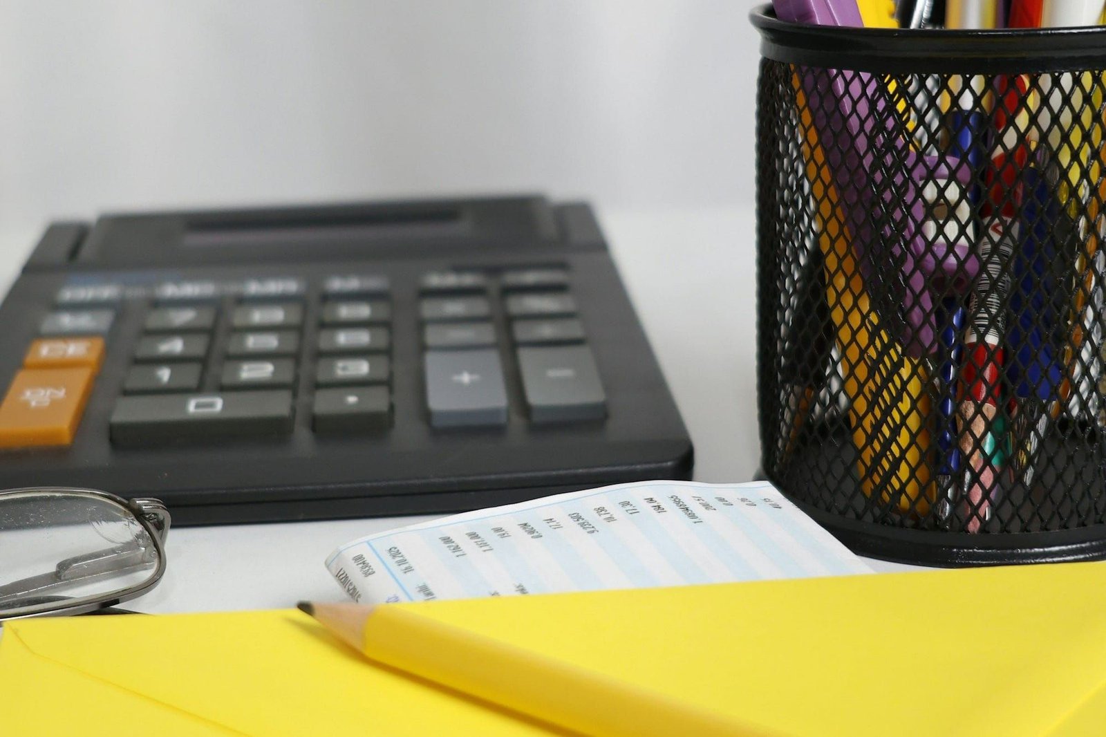 A desk with a calculator, a pot of pens, a pencil and a yellow envelope, ready for invoicing work