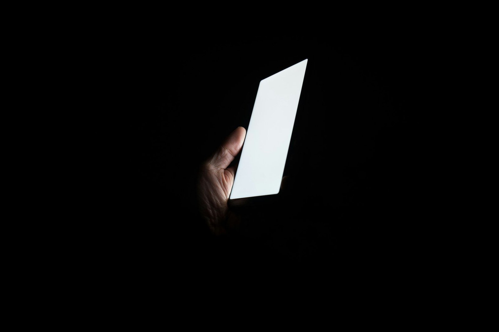 A hand holding a glowing smartphone in complete darkness