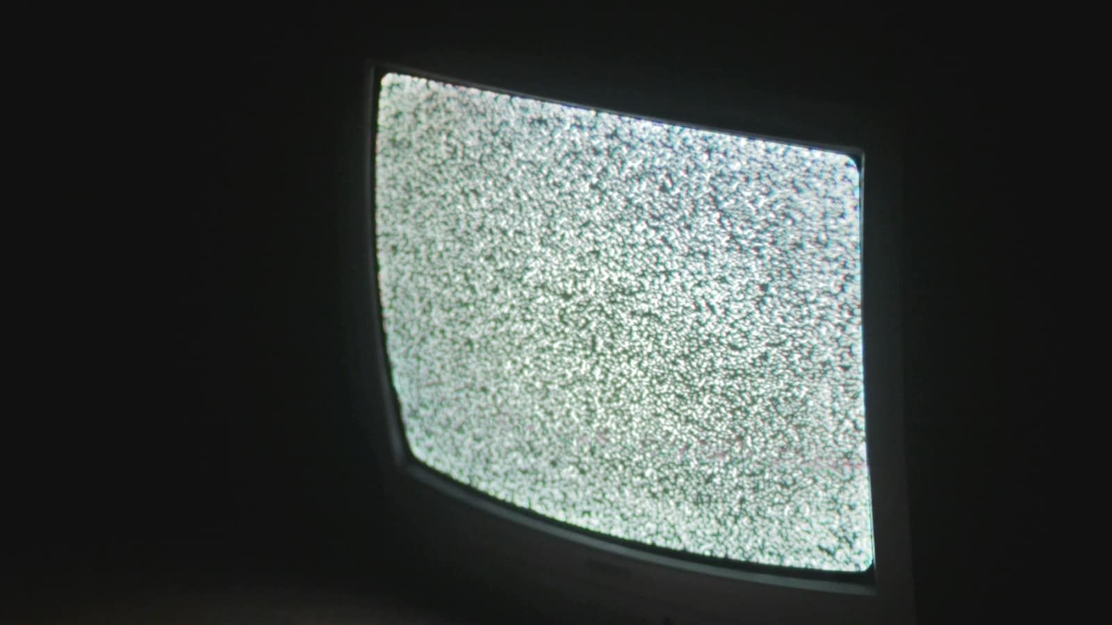 An old CRT television showing grey static in a dark room